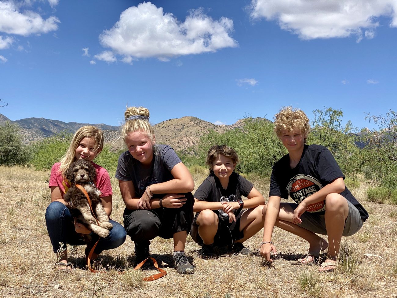 Kids crouching with Nine Nine, a bernedoodle puppy