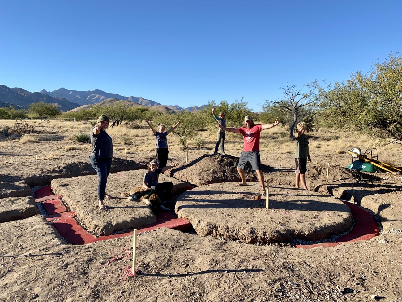 Family celebrating after laying the first layer of hyperdobe earthbags for their solar shed office.