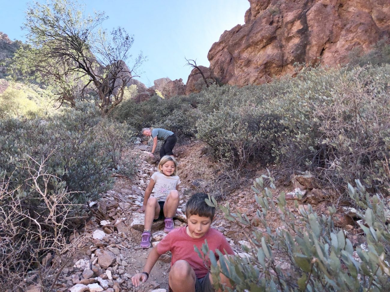 Three kids scooting down a steep rocky trail