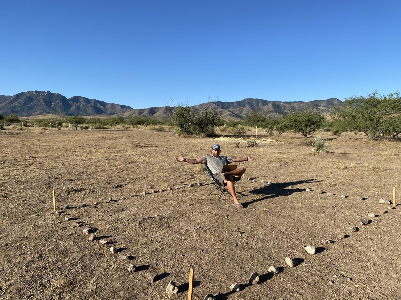 Jonathan sitting inside rock outline of what will eventually be a solar sed/office.